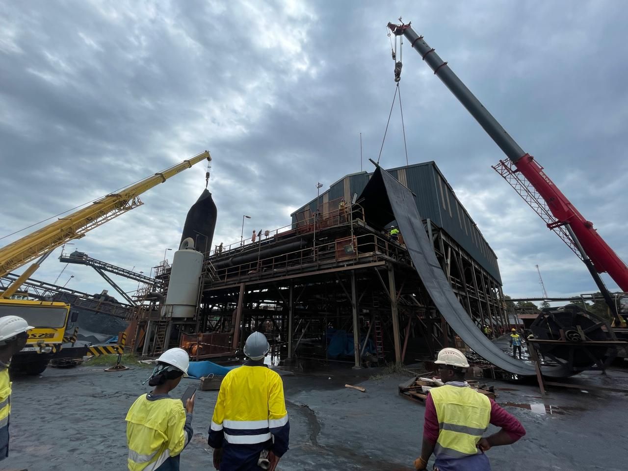 Conveyor belt installation work at an industrial site with cranes lifting belt sections